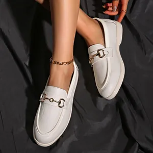 Detailaufnahme weißer Damen-Loafers mit goldener Trensenschnalle auf schwarzer Seide