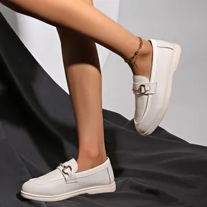 Nahaufnahme eleganter weißer Damen-Loafers mit goldener Schnalle an den Füßen des Models