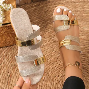 Detail view of women's glitter flat sandals with gold buckles on a straw mat