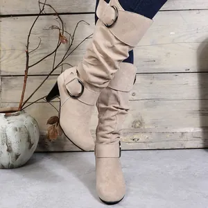 Detailed view of beige suede mid-calf boots with decorative metal buckle and high heel