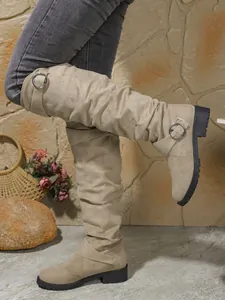 Λεπτομέρεια από μπεζ σουέτ μπότες Western με σούρες και κομψές μεταλλικές αγκράφες.