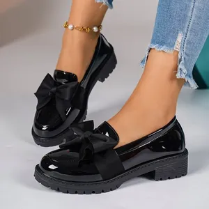 Detail view of black patent leather loafers with a large ribbon bow and thick sole.
