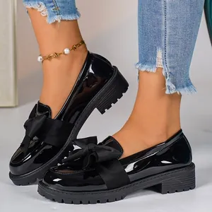 Detailed view of black patent leather loafers with decorative bow and thick sole