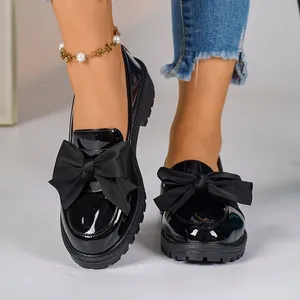 Close-up of black patent leather loafers with oversized bow and chunky platform sole.