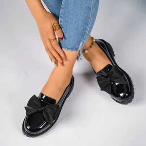 Black patent leather loafers with oversized fabric bows and platform soles on model