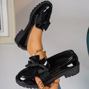 Close-up of black patent leather loafers with large ribbon bow and platform sole