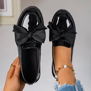 Close-up view of black patent leather loafers featuring a large bow and thick platform sole