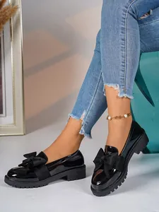 Detail of black patent leather loafers with a bow and platform sole on a model.