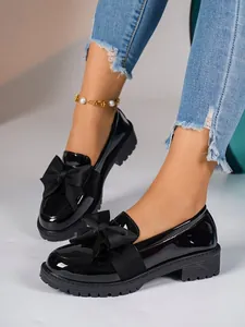 Close-up of black patent leather loafers with large bow detail and thick lug sole
