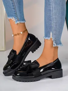 Close-up detail of stylish black patent leather loafers featuring a fabric bow and chunky lug sole