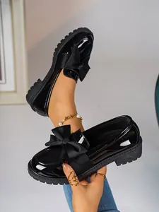 Detail shot of women's black patent leather loafers featuring a large decorative bow