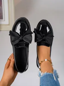 Elegant black patent leather loafers with a large bow detail and chunky vintage soles.