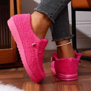 Close-up shot of hot pink fuzzy winter loafers worn on feet in a cozy home setting