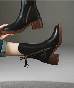 Detailed view of black leather ankle boots with side zipper and chunky wooden heel.