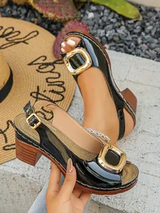 Close-up detail of black patent leather peep-toe sandals with gold buckle and chunky heel