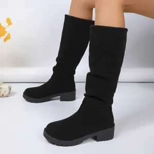 Side view of black suede slouchy knee-high boots with chunky heels and lug soles.