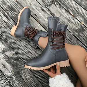Detail view of grey mid-calf knight boots with brown laces and metallic studs on wood