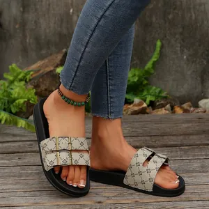 Close-up van dames slippers met dikke zool, dubbele gespen en monogram opdruk.