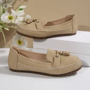 Close-up of beige women's loafers featuring decorative tassels and visible stitching detail.