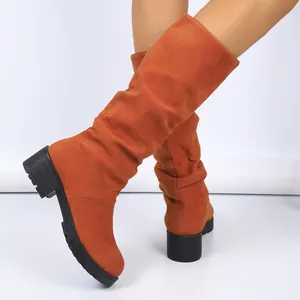 Detail shot of stylish orange suede slouchy mid-calf boots with chunky black heels