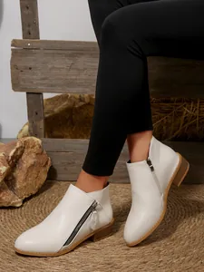 Close-up of white pointed-toe ankle boots with dual zippers and block heels for women.