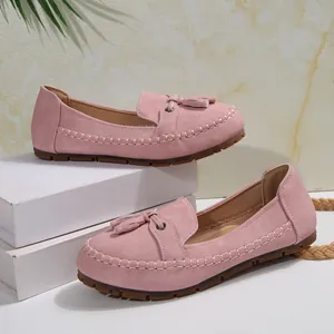 Close-up detail view of pink suede loafers with decorative tassels on white display platform