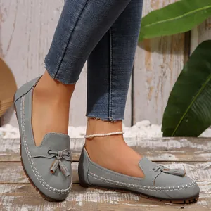 Close-up of grey women's tassel loafers with white stitching on wooden floor.