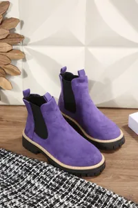 Dettaglio ravvicinato di stivaletti Chelsea in pelle scamosciata viola con suola spessa.