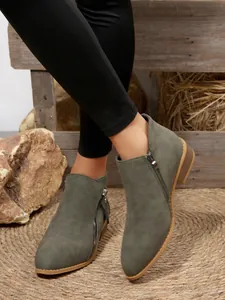 Close-up detail of grey-green pointed toe ankle boots with double side zippers on a woven mat.