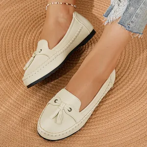 Detailansicht eleganter cremefarbener Damen-Loafer mit Quasten auf einer geflochtenen Matte
