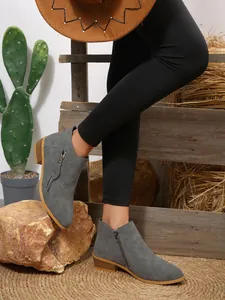 Close-up side view of grey pointed-toe ankle boots with dual metal zippers on rustic background.