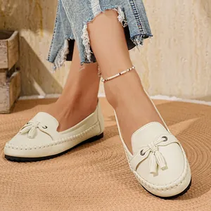 Nahaufnahme von cremefarbenen Damen-Loafers mit Quasten auf einem gewebten Teppich.