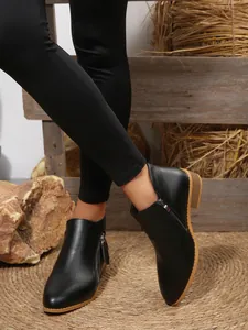 Close-up detail of black leather ankle boots featuring a pointed toe and double side zippers.