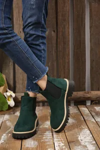Stivaletti Chelsea da donna in camoscio verde indossati con jeans su sfondo di legno