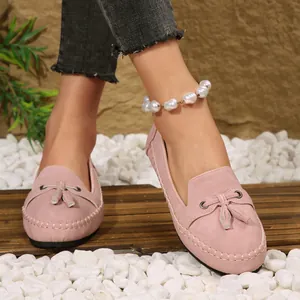 Detail view of pink suede loafers with decorative tassels and stitching on foot