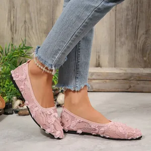 Detailed view of pink lace flat shoes with 3D floral accents worn on feet