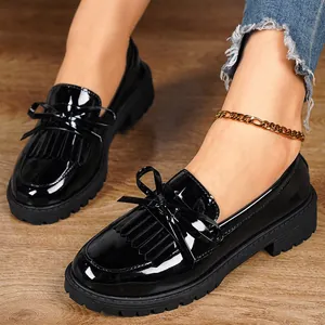 Close-up detail of black patent leather loafers with bow and fringe on wooden floor.