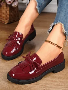 Close-up of stylish wine red patent leather loafers with elegant bow and tassel details