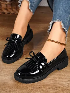 Close-up detail of black patent leather loafers with bow and tassel worn with denim