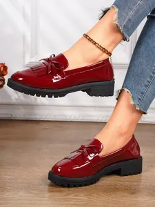 Close-up of elegant red patent leather loafers with fringe bow detail worn by a model