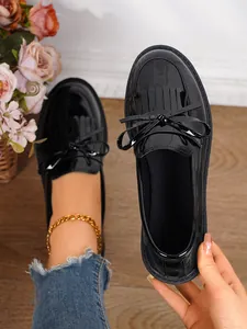 Detailed view of black patent leather loafers featuring a bow and fringe detail.