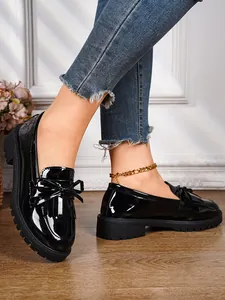 Close-up detail of stylish black patent leather loafers featuring a bow and fringe design