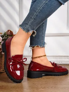 Detailed close-up shot of burgundy patent leather loafers with bow and fringe details