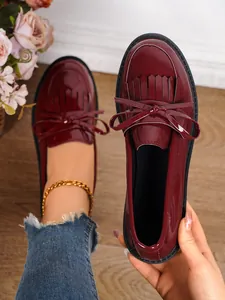 Close-up of stylish burgundy patent leather loafers featuring fringe and bow details