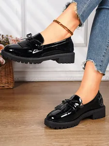 Detail showing glossy black patent leather loafers with delicate bow and tassel accents.