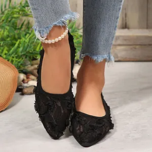 Close-up of black lace pointed-toe flat shoes with 3D floral details worn by model