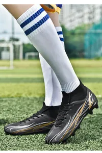 A professional close-up shot of black and gold high-top soccer cleats on grass.