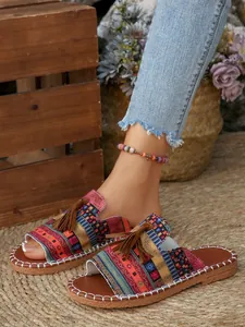 Bohemian flat slides with colorful woven patterns and decorative tassels on straw mat.