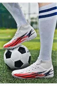 Close-up view of white high-top soccer shoes with red and navy blue patterns on turf.