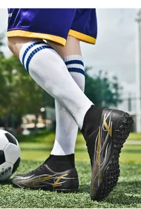 Close-up view of high-top soccer cleats featuring gold flame patterns and TF turf soles